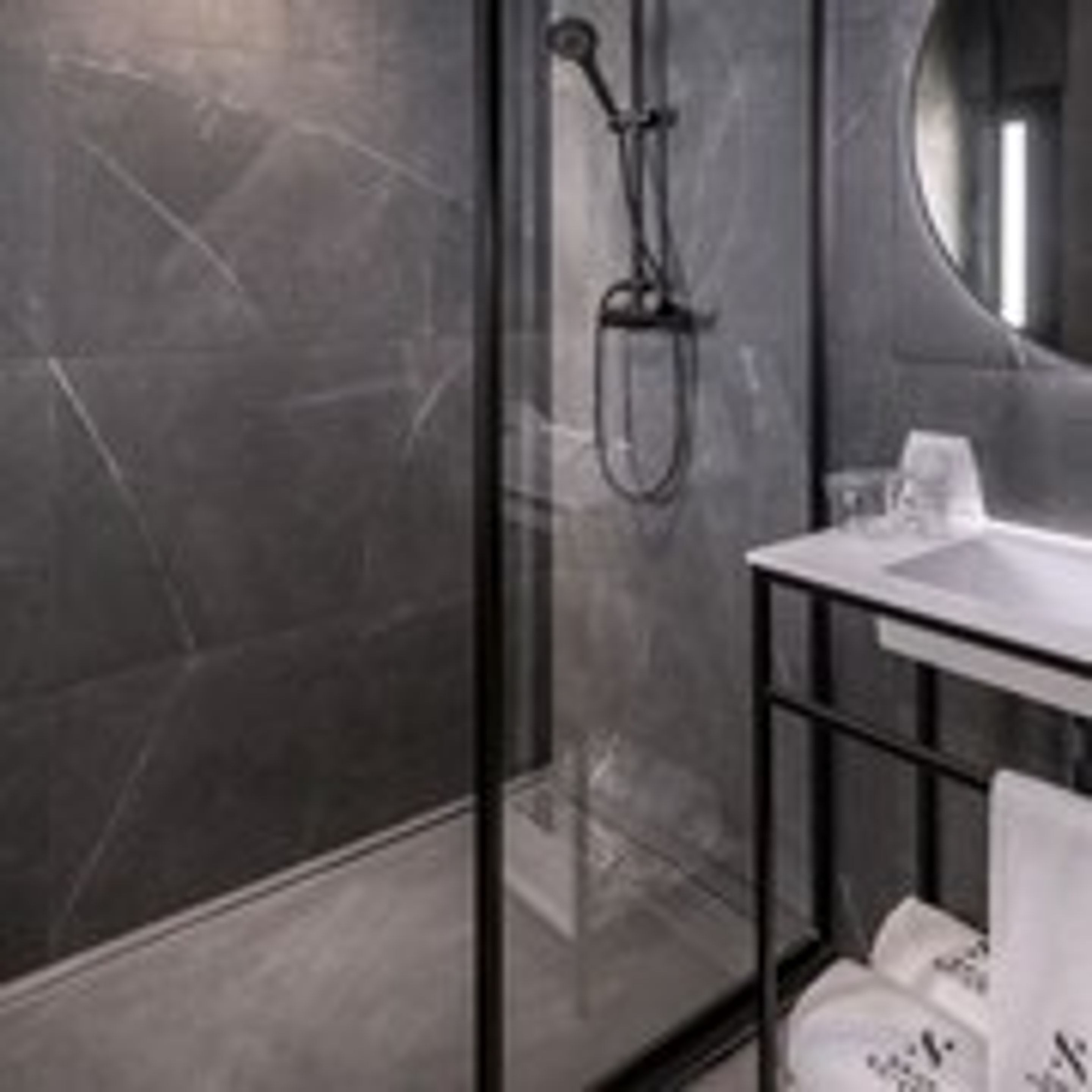 A modern bathroom with a glass shower enclosure, a white sink, and a round mirror.