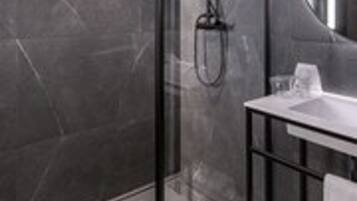 A modern bathroom with a glass shower enclosure, a white sink, and a round mirror.