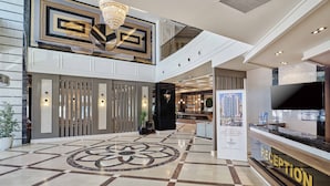 Un hall d’hôtel comprenant un comptoir d’accueil, un lustre et un motif décoratif sur le sol.