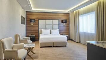Habitación de hotel moderna con una cama grande, dos mesitas de noche, un escritorio, una silla y un amplio ventanal con cortinas.