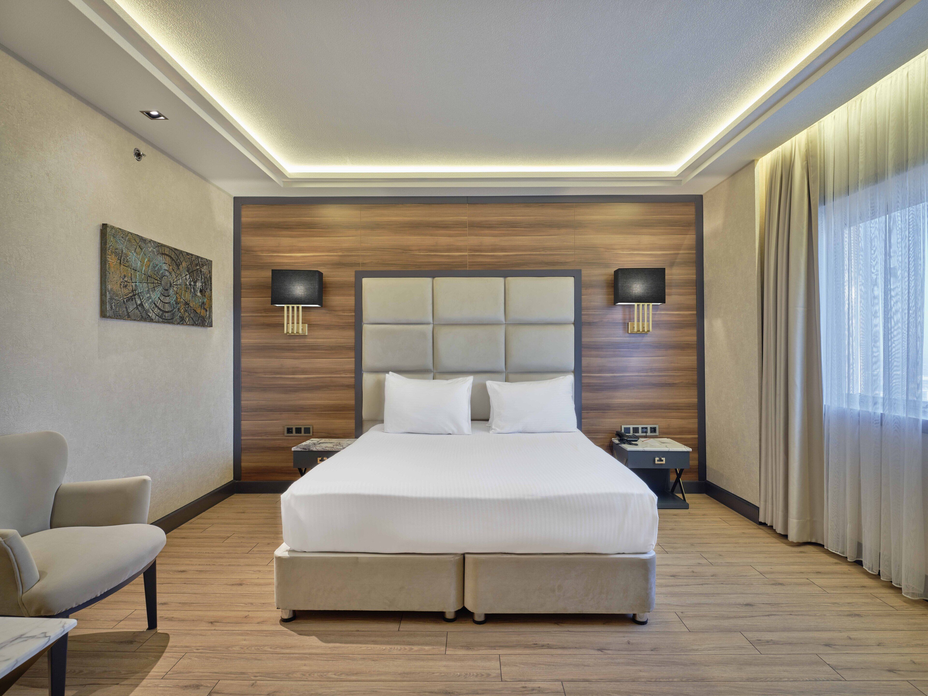 Een moderne hotelkamer met een groot bed, twee nachtkastjes, een stoel en een schilderij aan de muur.