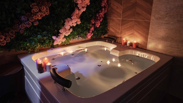 Un espace de détente avec une grande baignoire entourée de bougies et de pétales de rose.