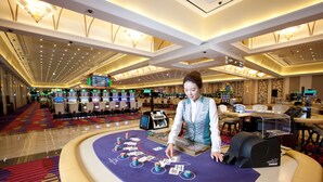 A casino floor with multiple gaming tables, a woman playing blackjack, and a variety of slot machines. - High1 Grand Hotel Main Tower (Jeongseon)