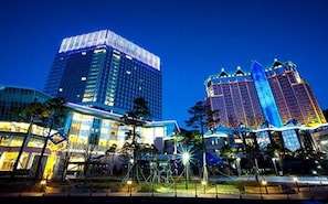 A modern urban skyline with high-rise buildings, including a prominent glass skyscraper and a hotel with a distinctive red and blue facade.