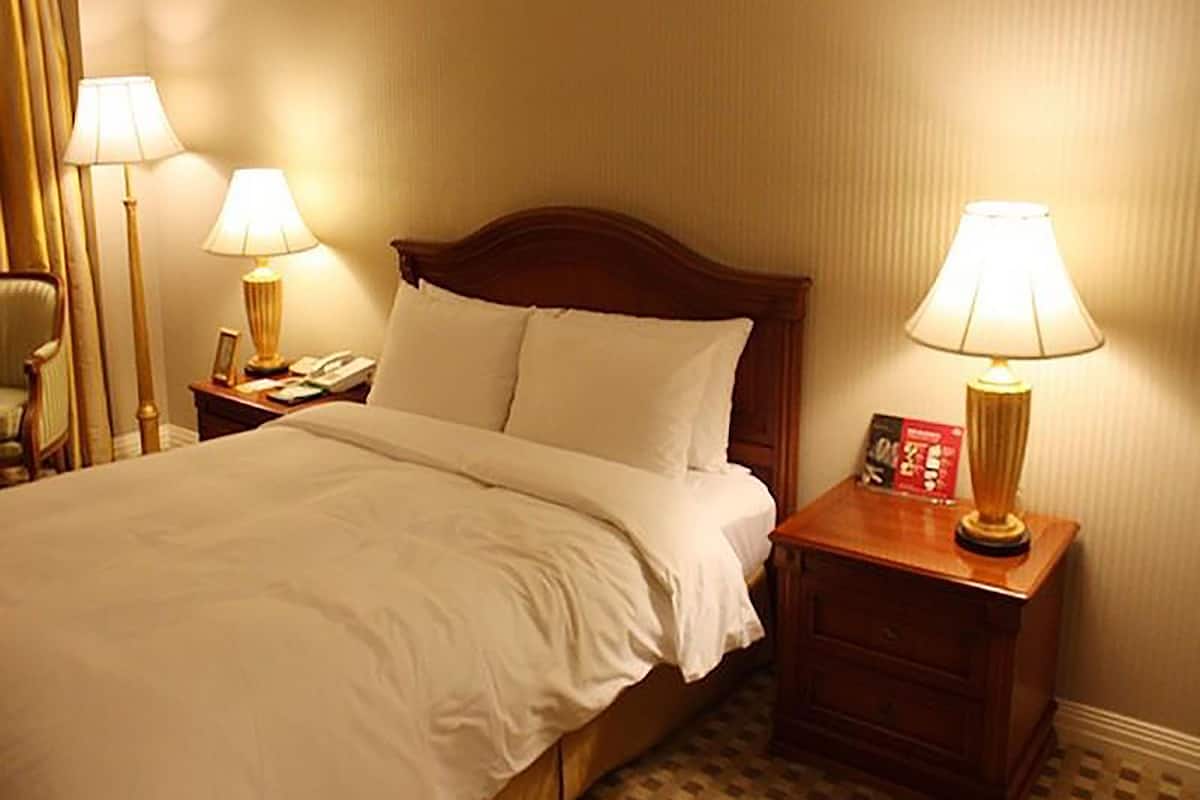 Ett hotellrum med en stor säng, två sängbord med lampor, en stol och ett litet bord med en telefon och en bok.
