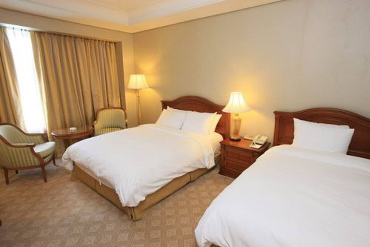 Ett hotellrum med två sängar, en stol, en lampa och en telefon på ett sidobord.