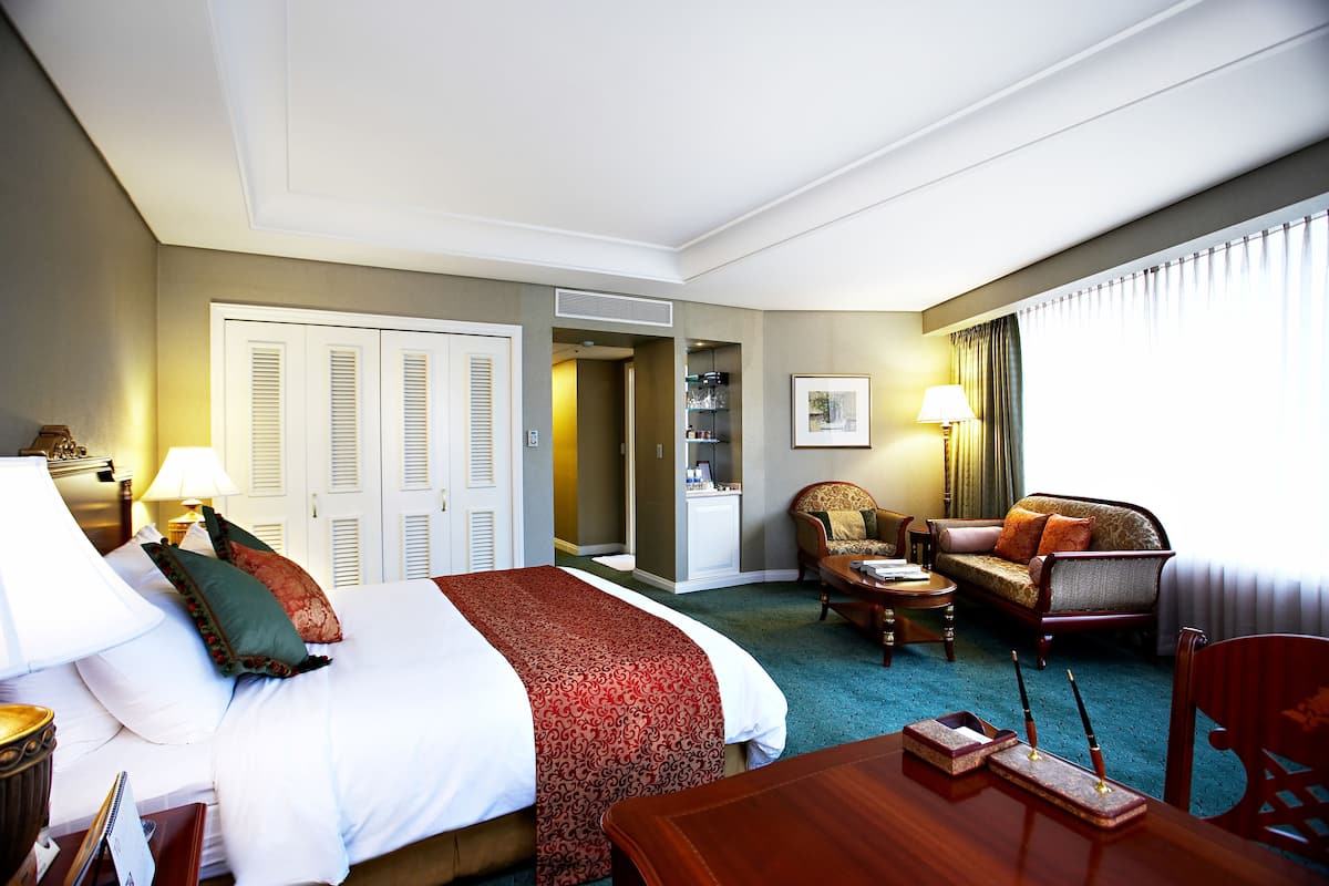 Ett hotellrum med en stor säng, en soffa, ett matbord och en stol. Det finns en dörr som leder till ett badrum och en garderob.