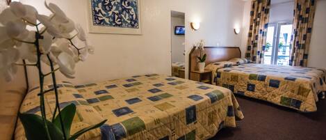 A hotel room with two beds, a potted orchid, a framed artwork, a television, and a window with curtains.