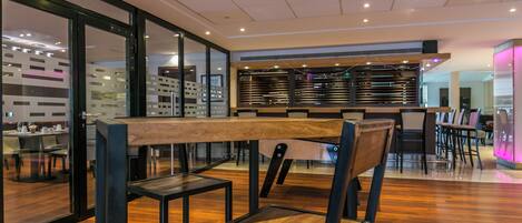 A modern restaurant with wooden flooring, black metal chairs, and a long wooden table.