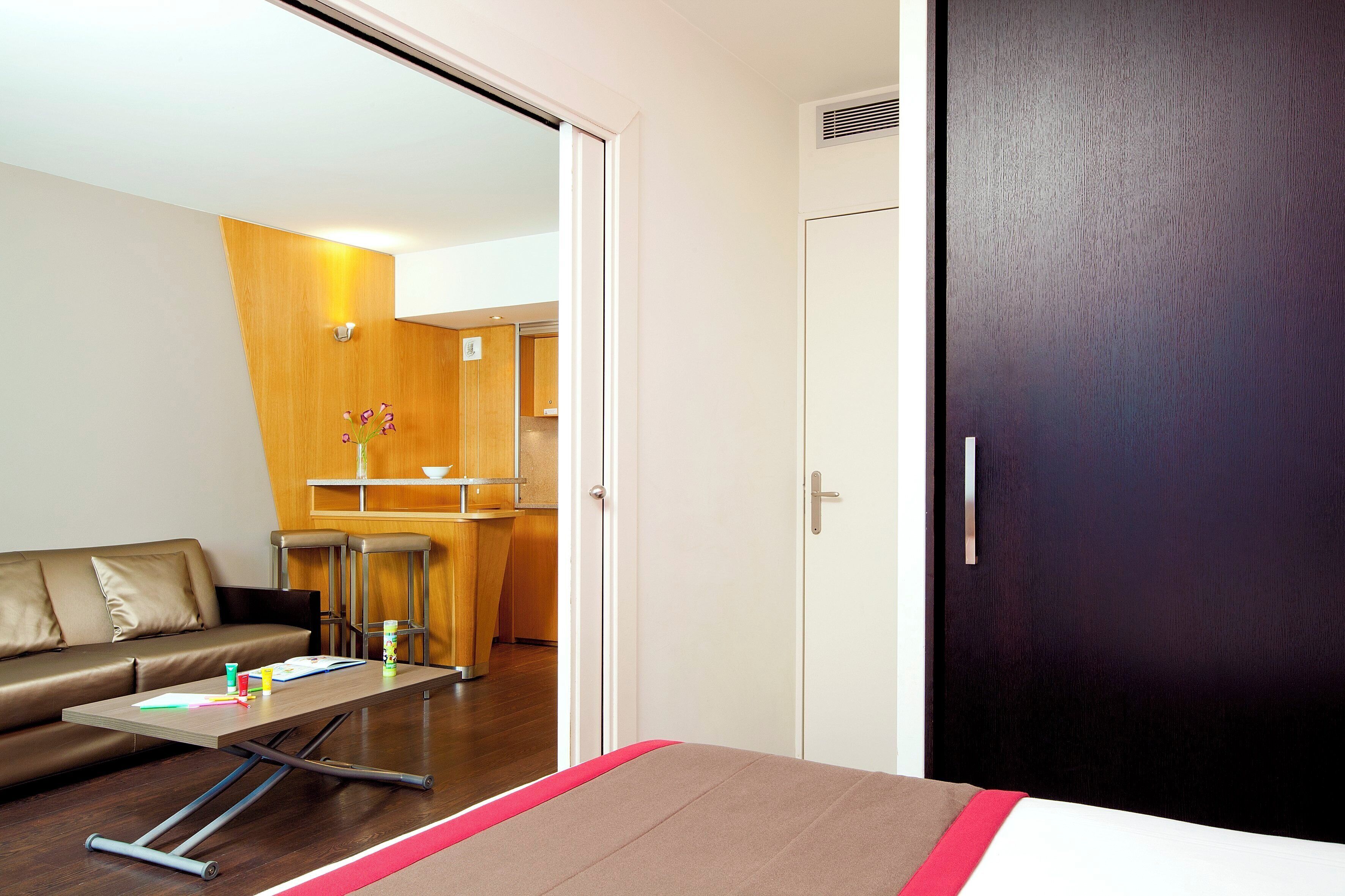 Una habitación de hotel moderna con cama, sofá, una mesita y una pequeña cocina.