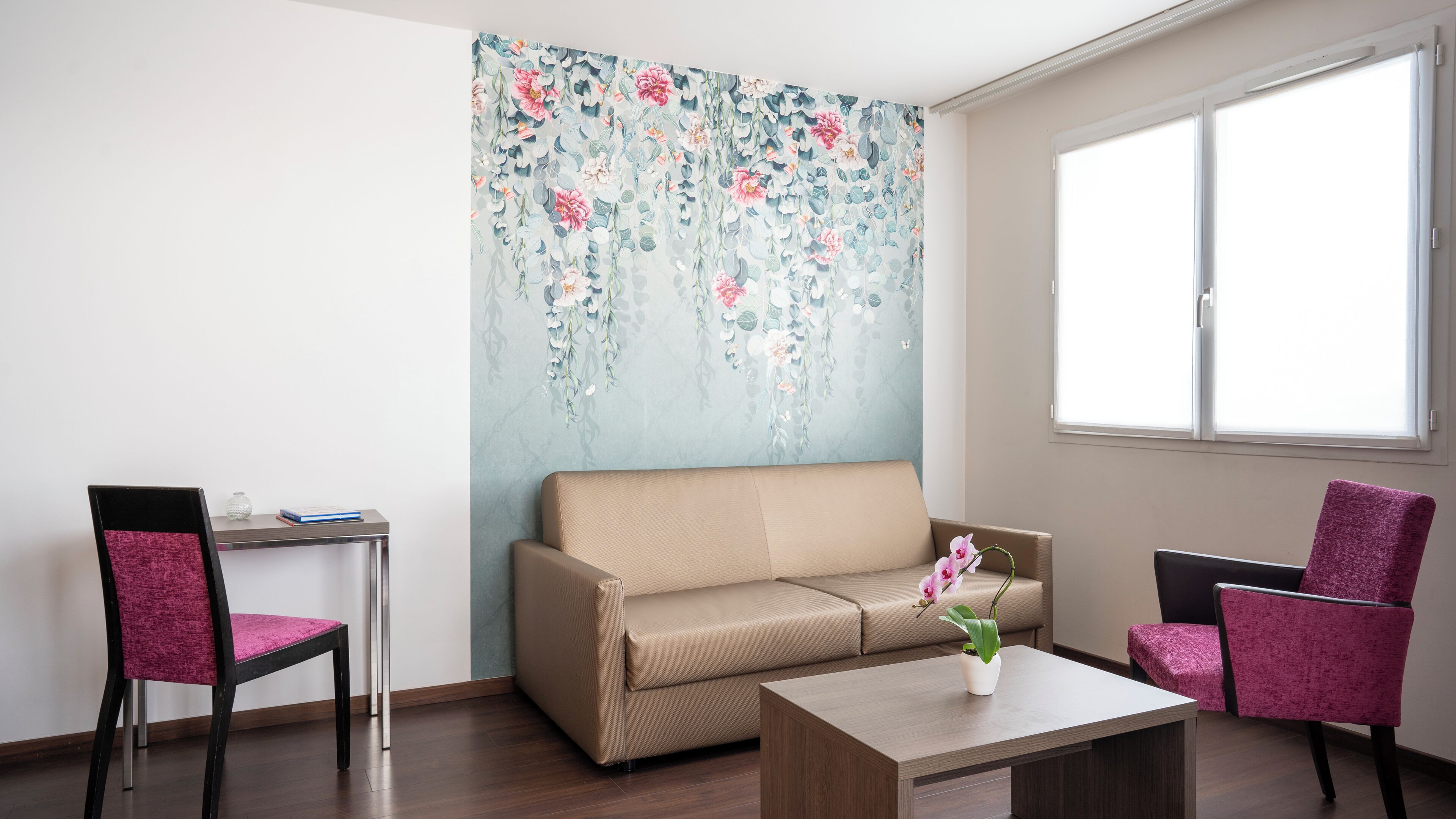 A modern living room with a beige sofa, two chairs, a coffee table, and a floral tapestry on the wall.