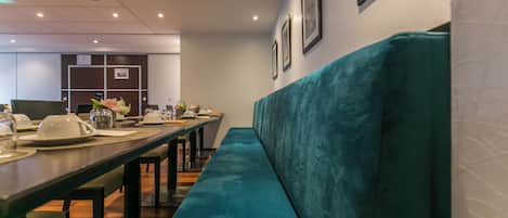A restaurant with a long table, teal cushioned bench, and framed pictures on the wall.