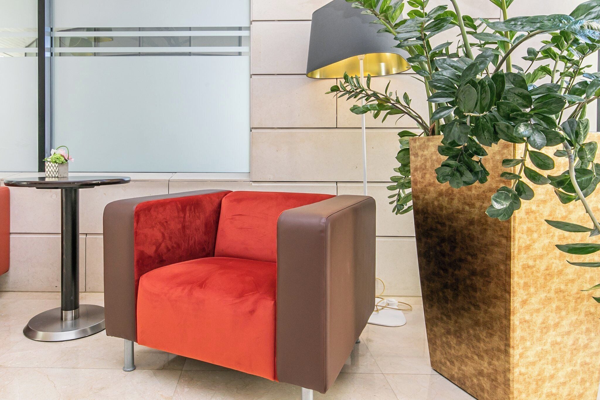 Un área de descanso moderna con un sillón rojo, una lámpara de pie y una planta grande en maceta.