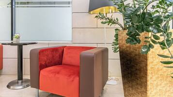 A modern lounge area with a red armchair, a floor lamp, and a large potted plant.