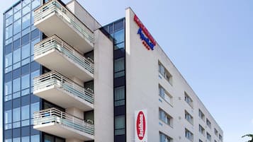 Un hôtel moderne doté d’une façade en verre, de nombreux balcons et d’une enseigne rouge et bleue bien visible.