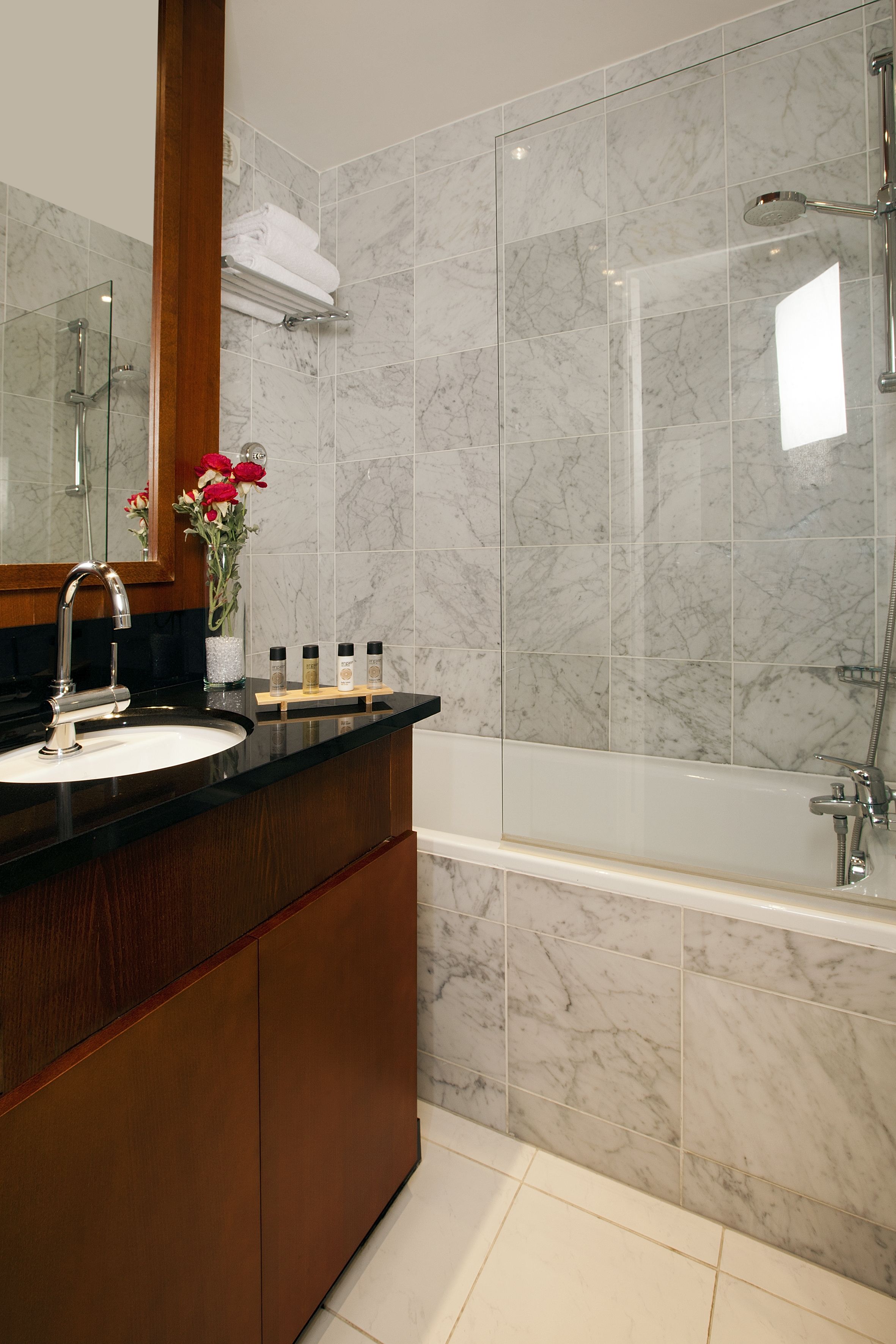 A modern bathroom with a marble-tiled shower, a wooden vanity with a sink, and a mirror above the vanity.
