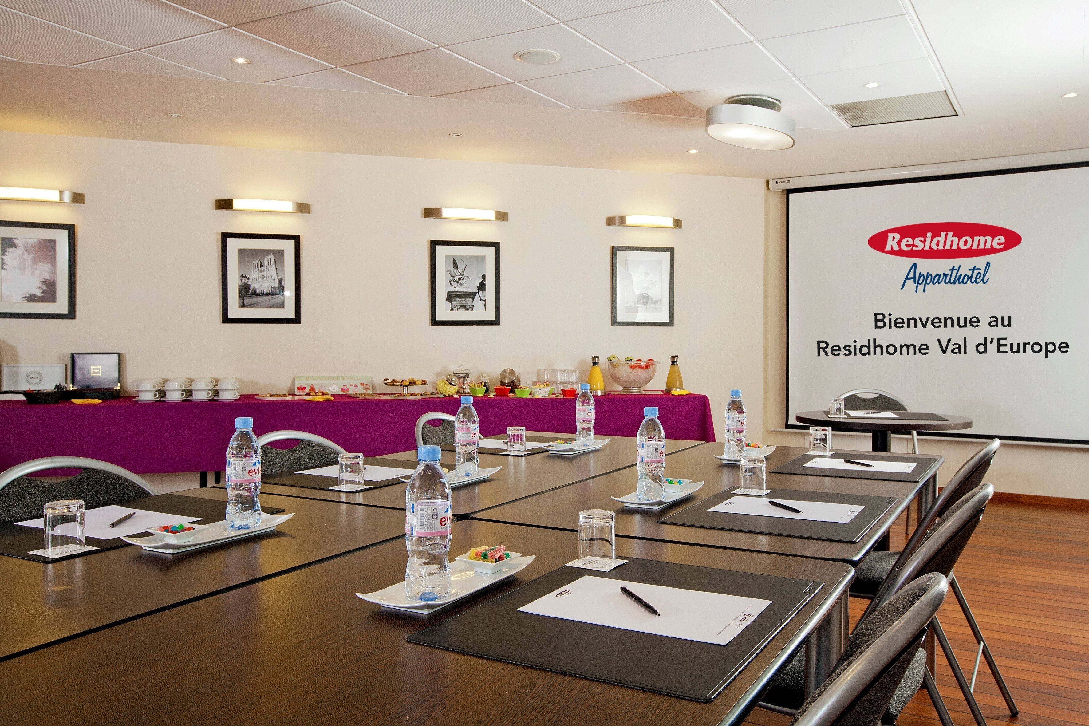 Een vergaderruimte met tafels klaar voor vergaderingen, waterflesjes en een presentatiescherm waarop 'Residhome Apparthotel' staat.