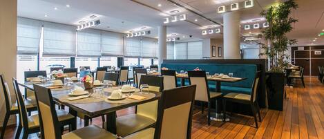 Un restaurante espacioso con suelo de madera, varias mesas de comedor con sillas y grandes ventanales que dejan entrar luz natural.