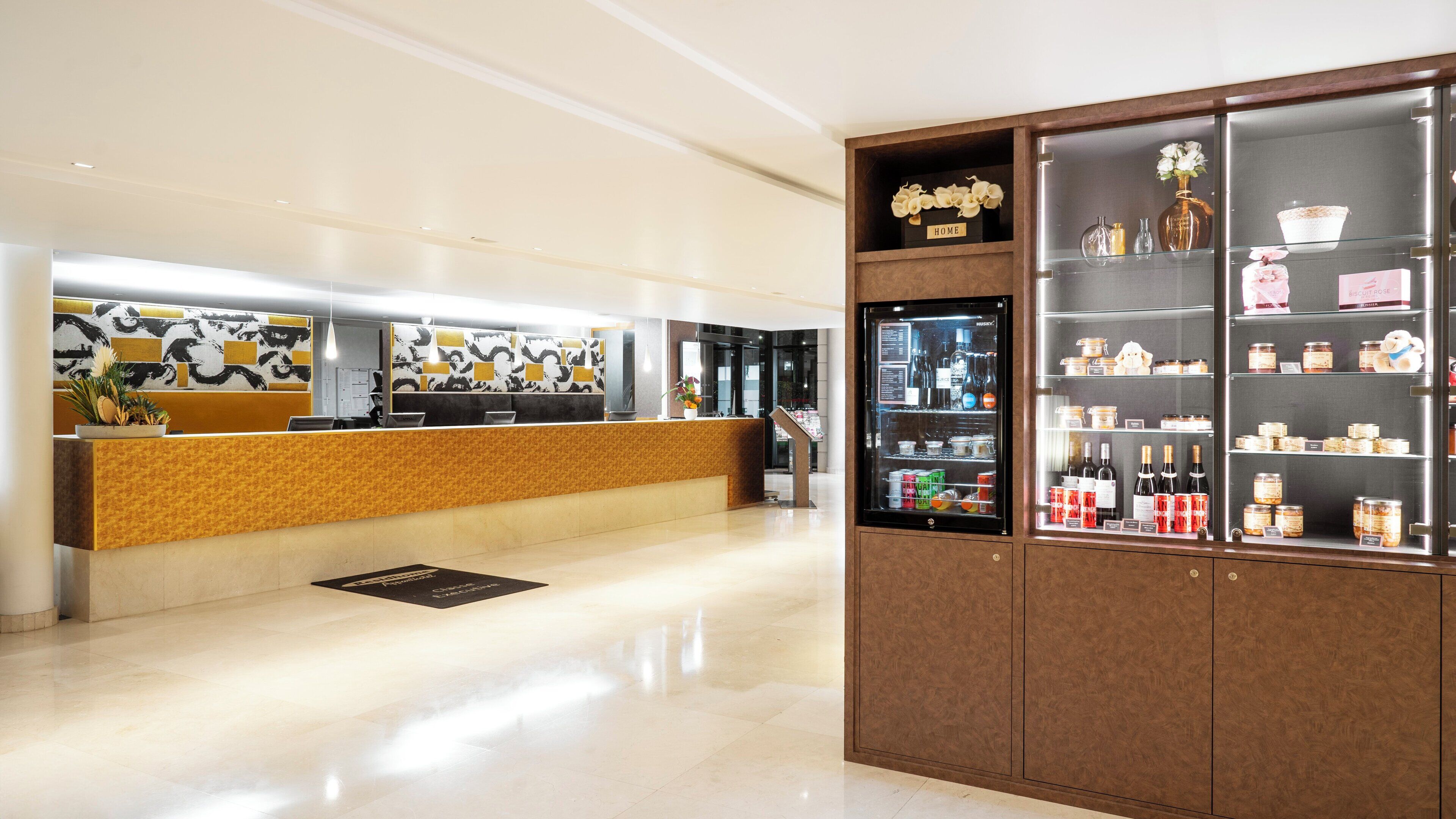 Eine Hotelrezeption mit modernem Design, inklusive einer Rezeptionstheke, einer Vitrine mit verschiedenen Gegenständen und einer Wand mit geometrischem Muster.