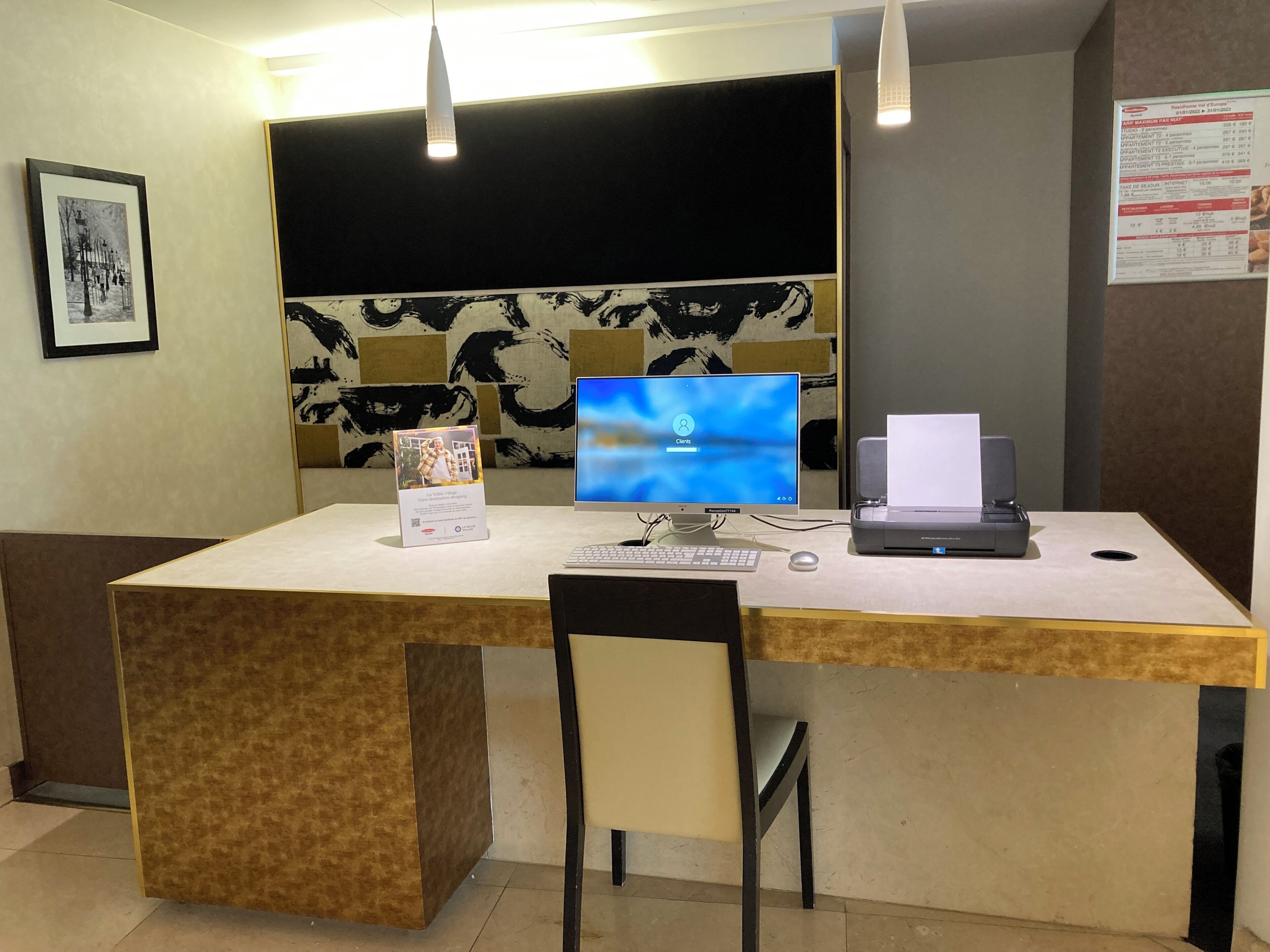 A reception desk with a computer, printer, and a framed picture on the wall.