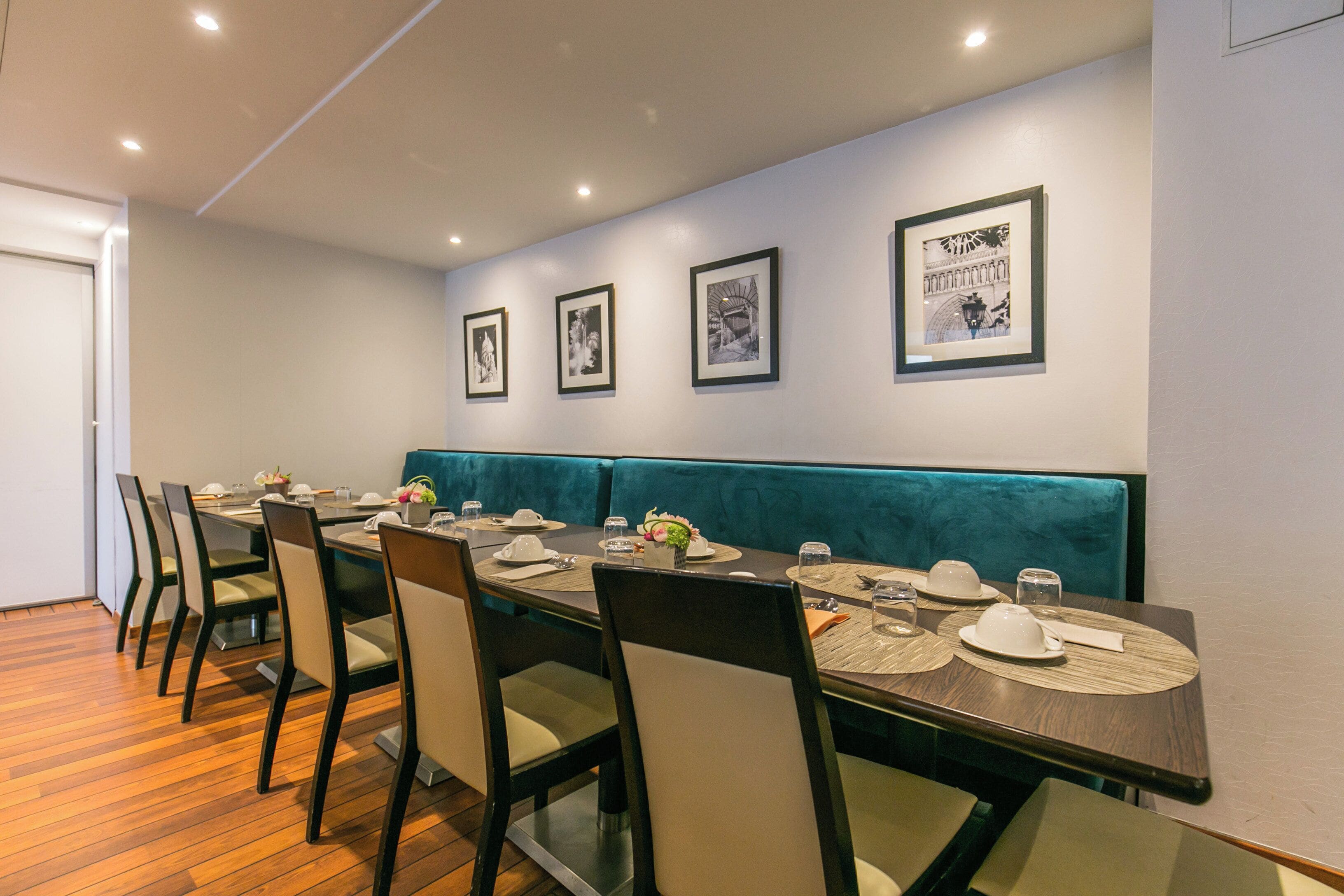 Un restaurante con una mesa larga dispuesta para comer, cuadros en la pared y una cabina color turquesa.