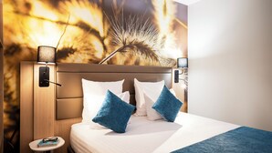 Habitación de hotel con una cama, dos almohadas, una mesita de noche, una lámpara y una obra de arte en la pared.