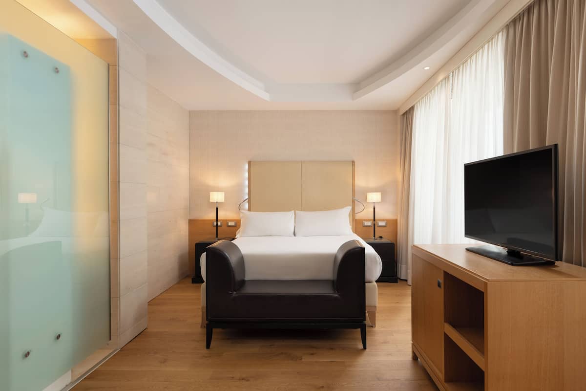 A modern hotel room with a bed, a TV on a wooden console, and two bedside lamps.
