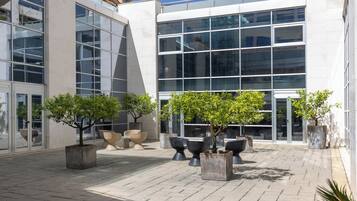 A modern building with large glass windows and a paved courtyard with potted trees and seating areas.