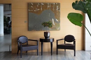 Un'area reception con due sedie nere, un piccolo tavolino rotondo con una pianta in vaso e un grande quadro astratto appeso al muro.