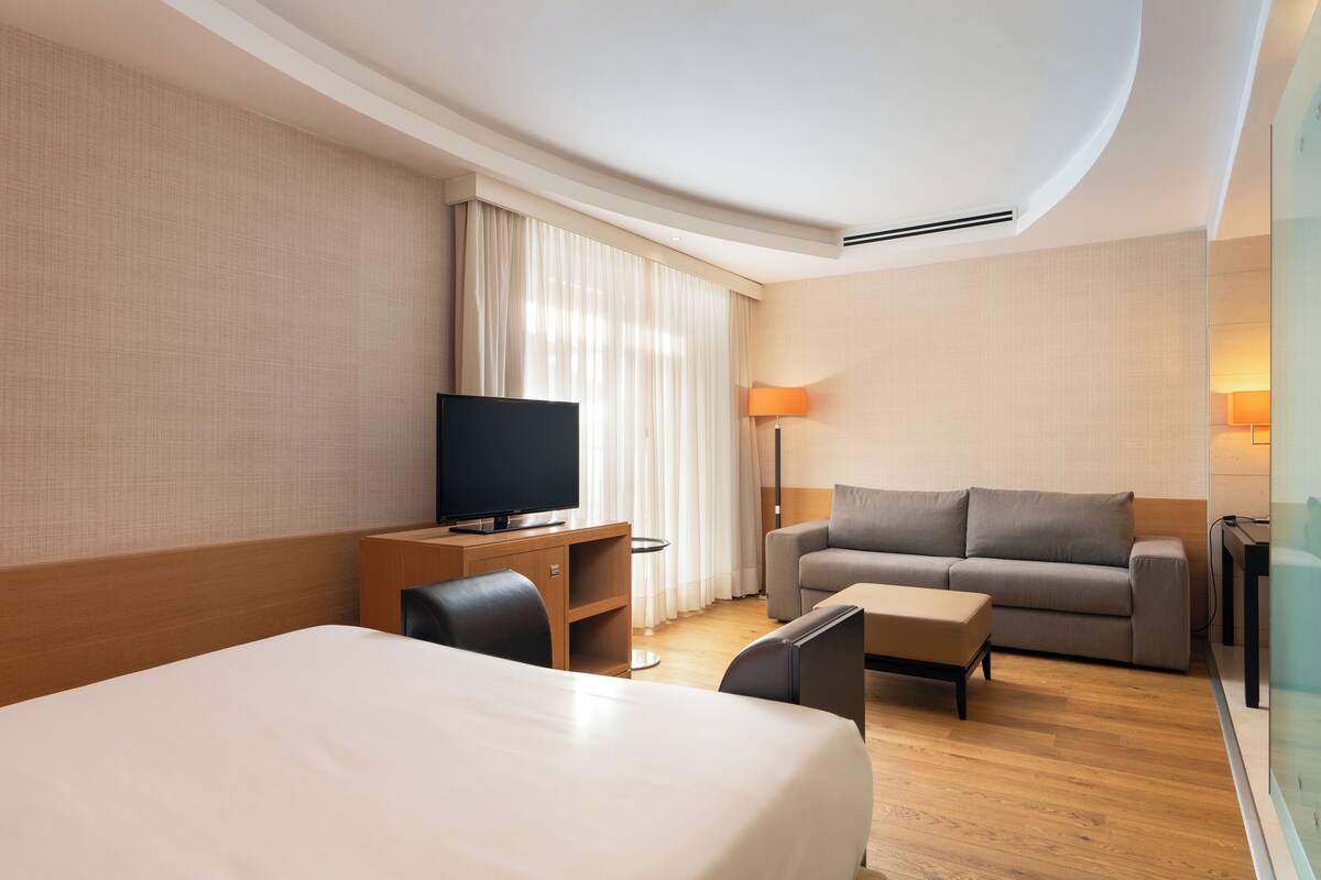 A hotel room with a large bed, a TV, a sofa, a small table, and a desk.