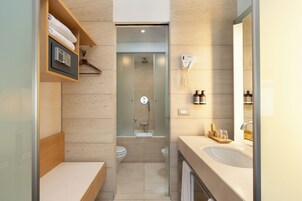 A modern bathroom with a shower, toilet, and sink. There is a towel rack with towels, a phone, and a soap dispenser.
