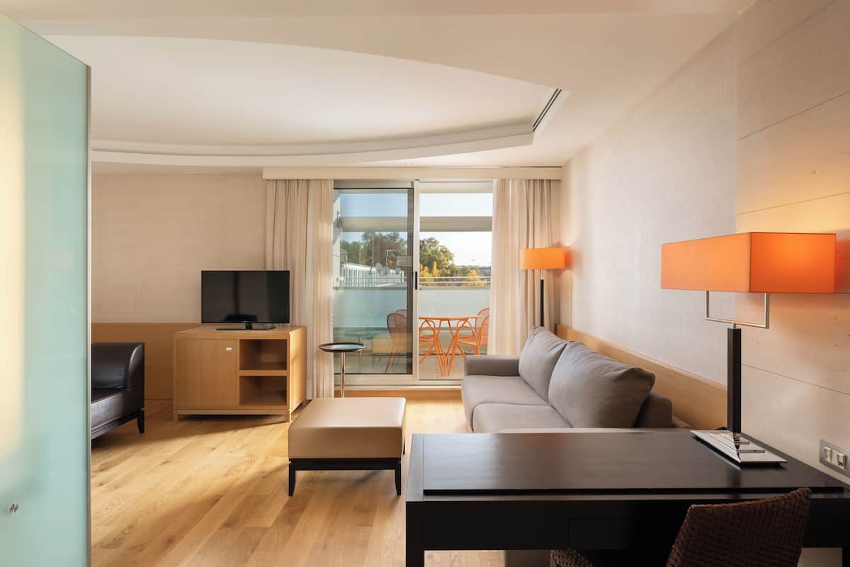 A modern hotel room with a sofa, a table, a TV, and a balcony with a view.