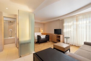 Une chambre d’hôtel moderne équipée d’un lit, d’un bureau, d’une télévision, d’un canapé et d’une salle de bain avec douche et miroir.