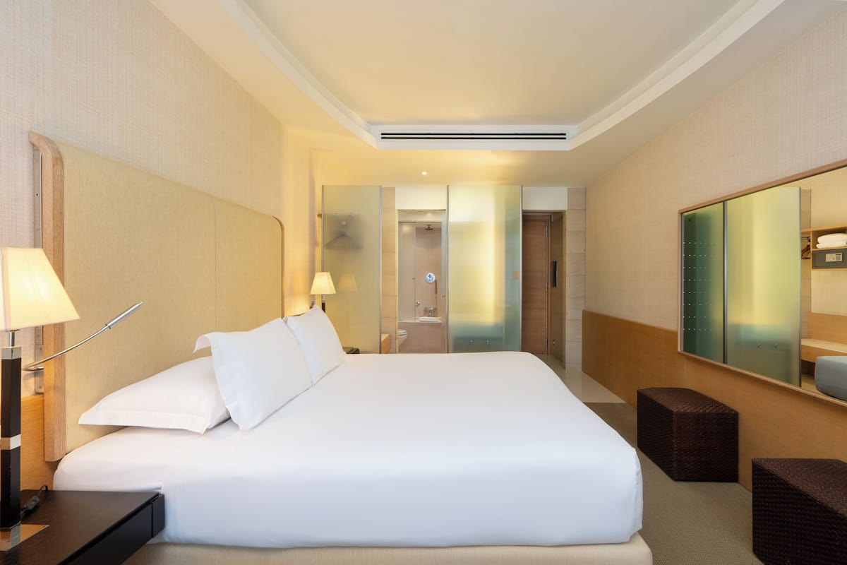 A hotel room with a large bed, bedside tables, a mirror, and a bathroom visible through a glass partition.