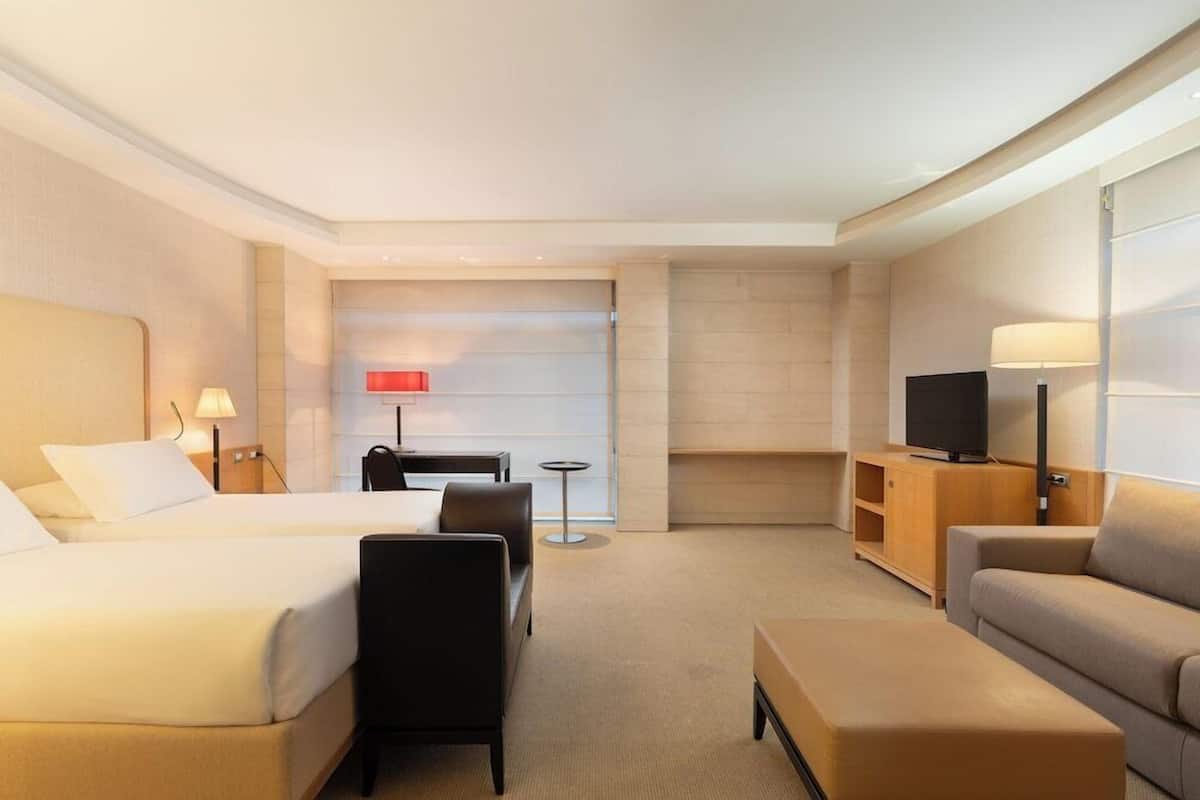 A hotel room with two beds, a sofa, a TV, a desk, and a lamp.