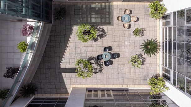 An aerial view of a courtyard with a central seating area, surrounded by potted plants and a glass facade. - Precise House Mantegna Roma (Rome)
