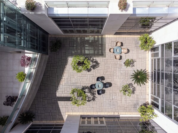 An aerial view of a courtyard with a central seating area, surrounded by potted plants and a glass facade. - Precise House Mantegna Roma (Rome)