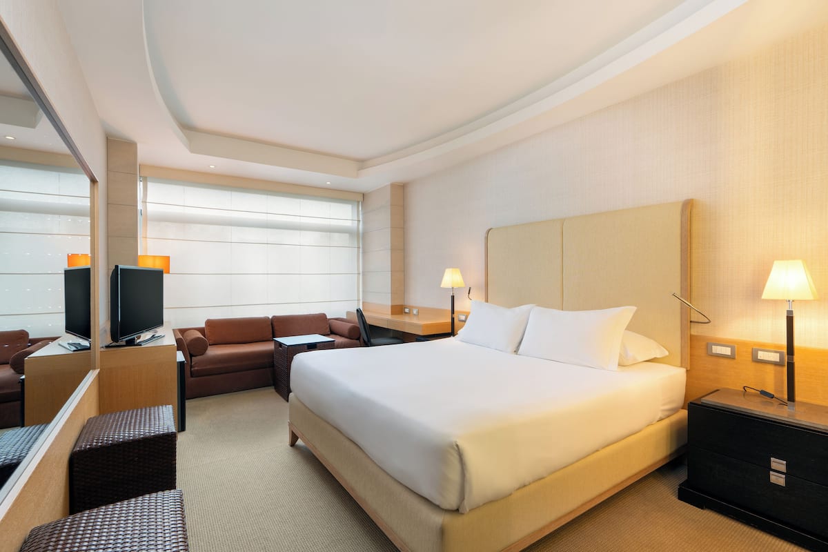 A hotel room with a large bed, a desk with a computer, a sofa, and a TV.