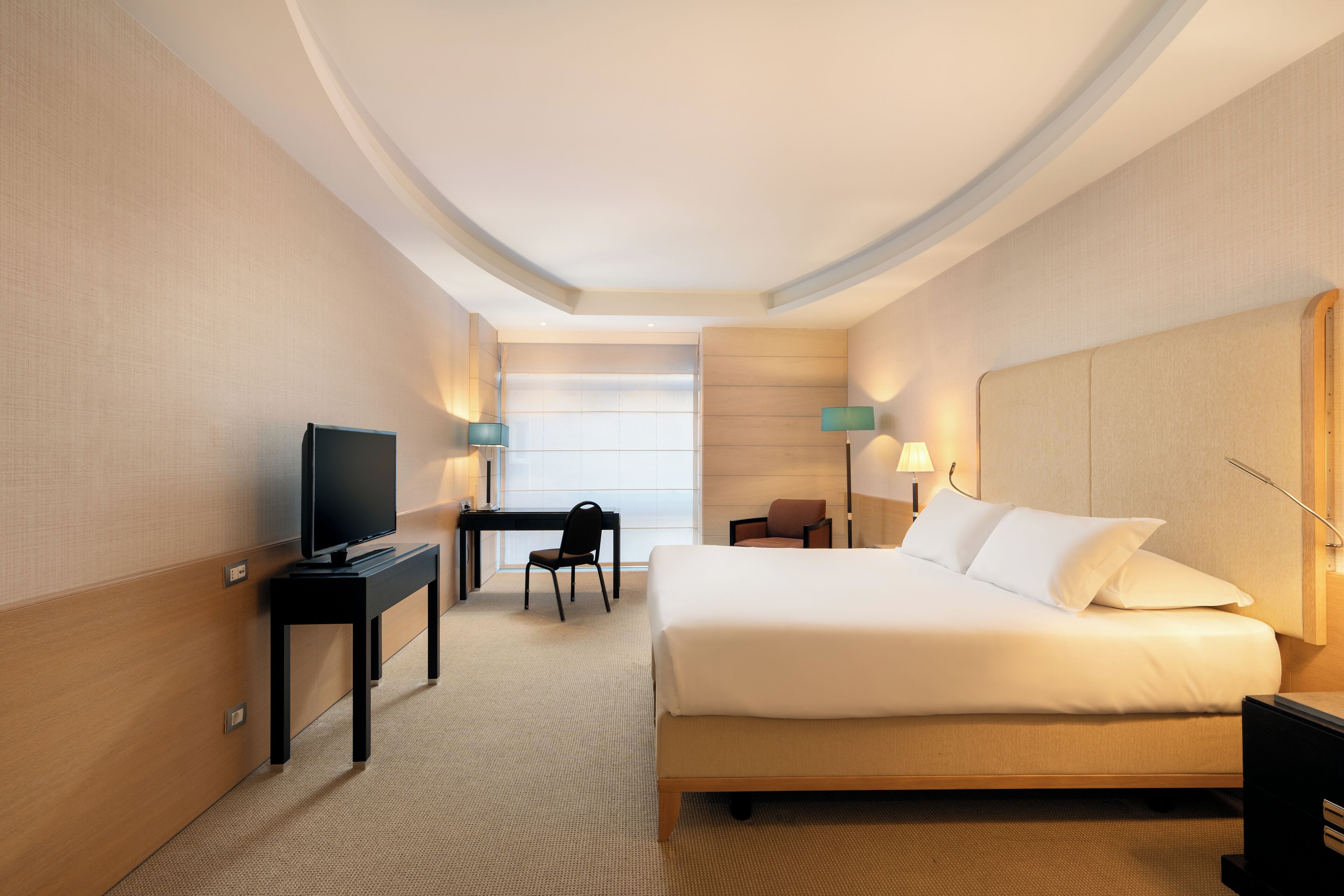 A hotel room with a large bed, a desk with a TV, and two chairs.