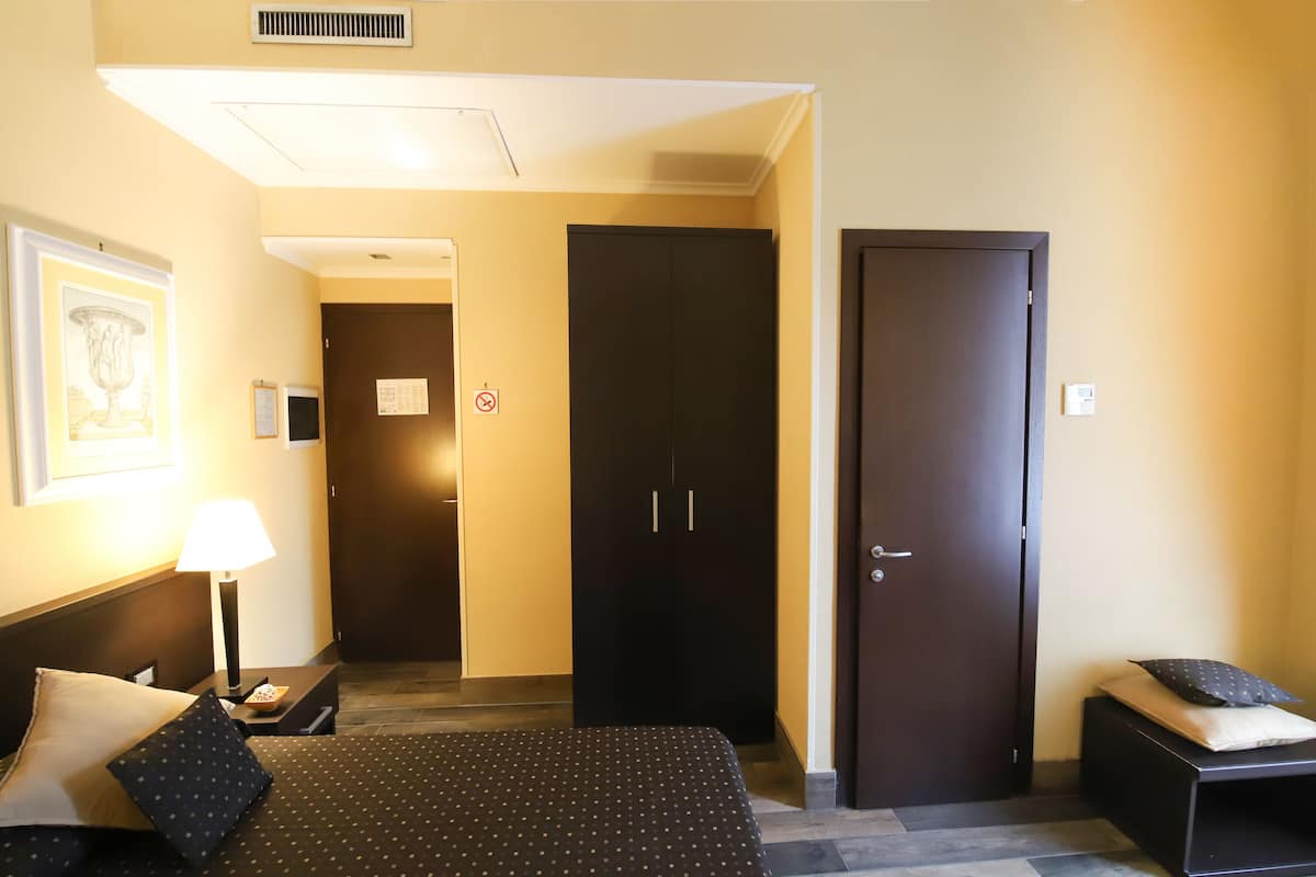 Una habitación de hotel con cama, mesita de noche, lámpara y armario.