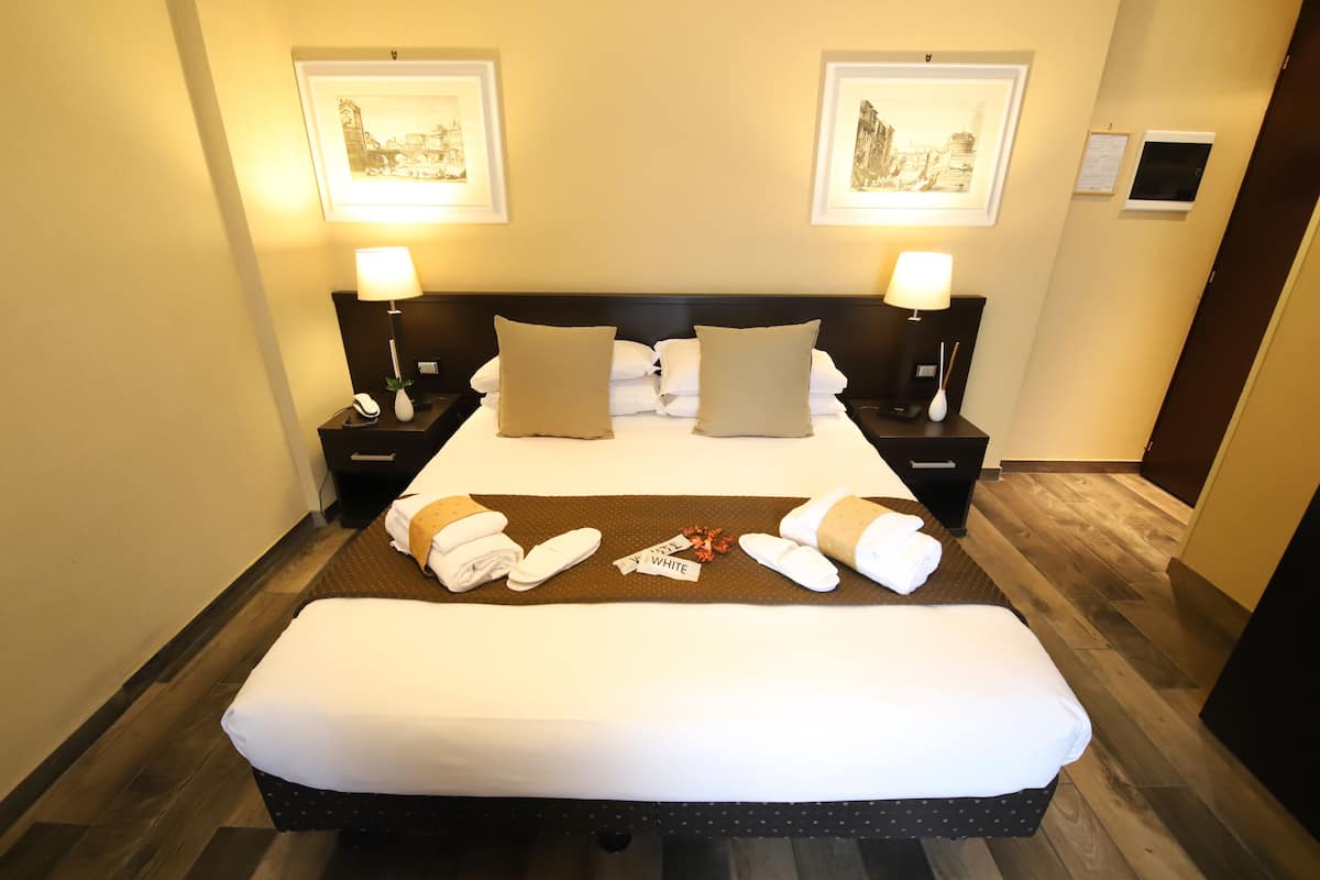 Habitación de hotel impecable con una cama grande, dos mesitas de noche con lámparas y obras de arte en las paredes.