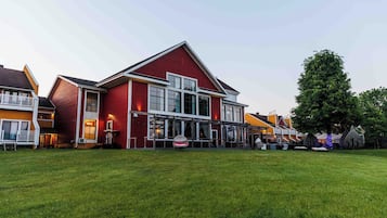 A red building with large windows and a balcony, surrounded by a grassy area and other buildings.