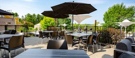 An outdoor patio with tables and chairs, umbrellas, and a view of trees and buildings.