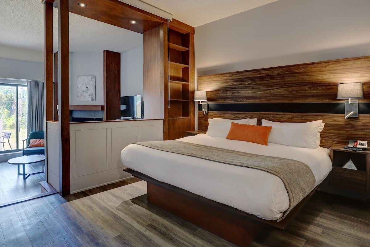 A modern hotel room with a large bed, wooden headboard, and a built-in desk with a television.
