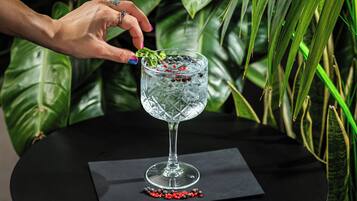 Une main dépose une feuille de menthe dans un verre contenant des glaçons et des baies de poivre rouge.