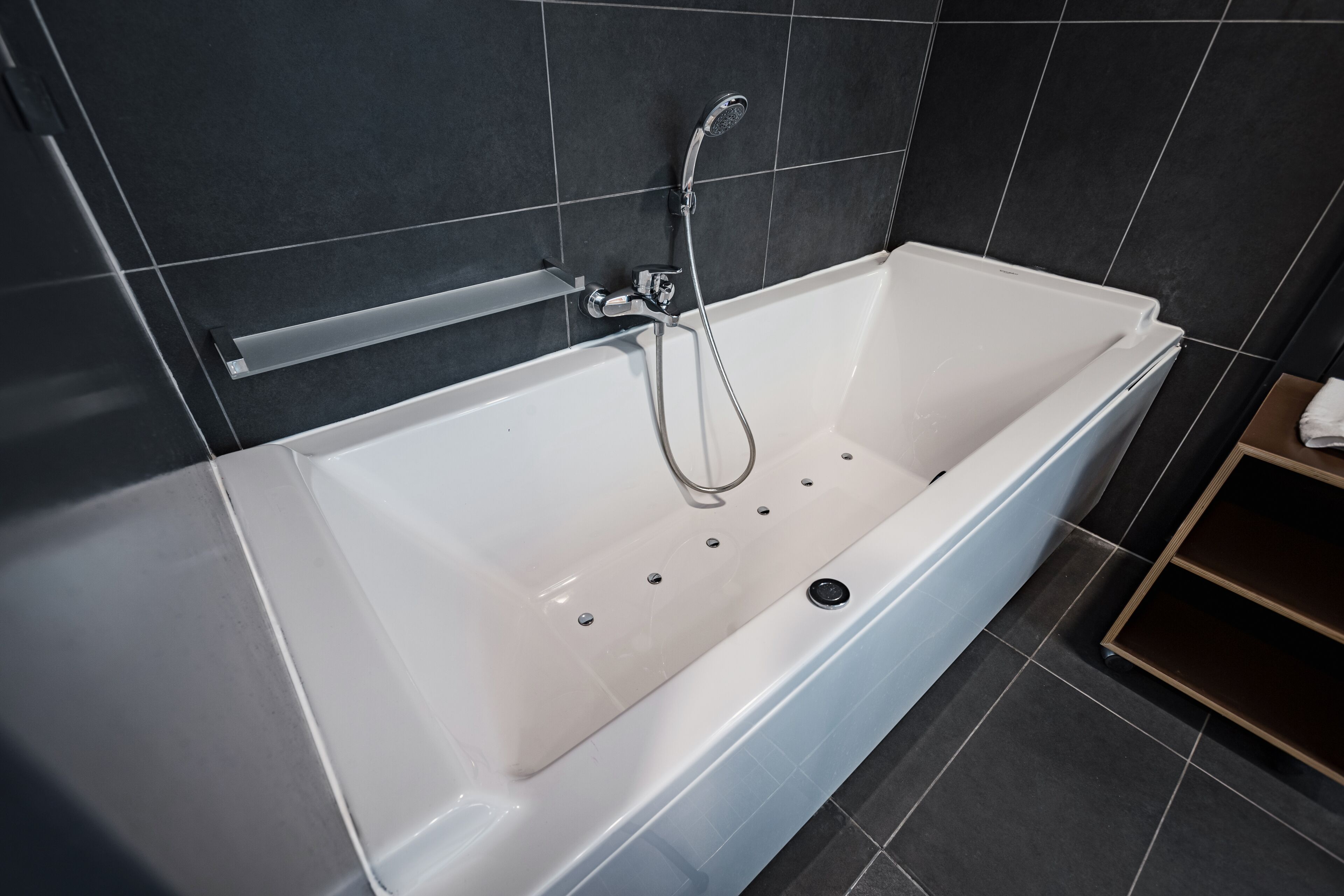 A modern bathroom with a white bathtub, a handheld showerhead, and a built-in shelf.