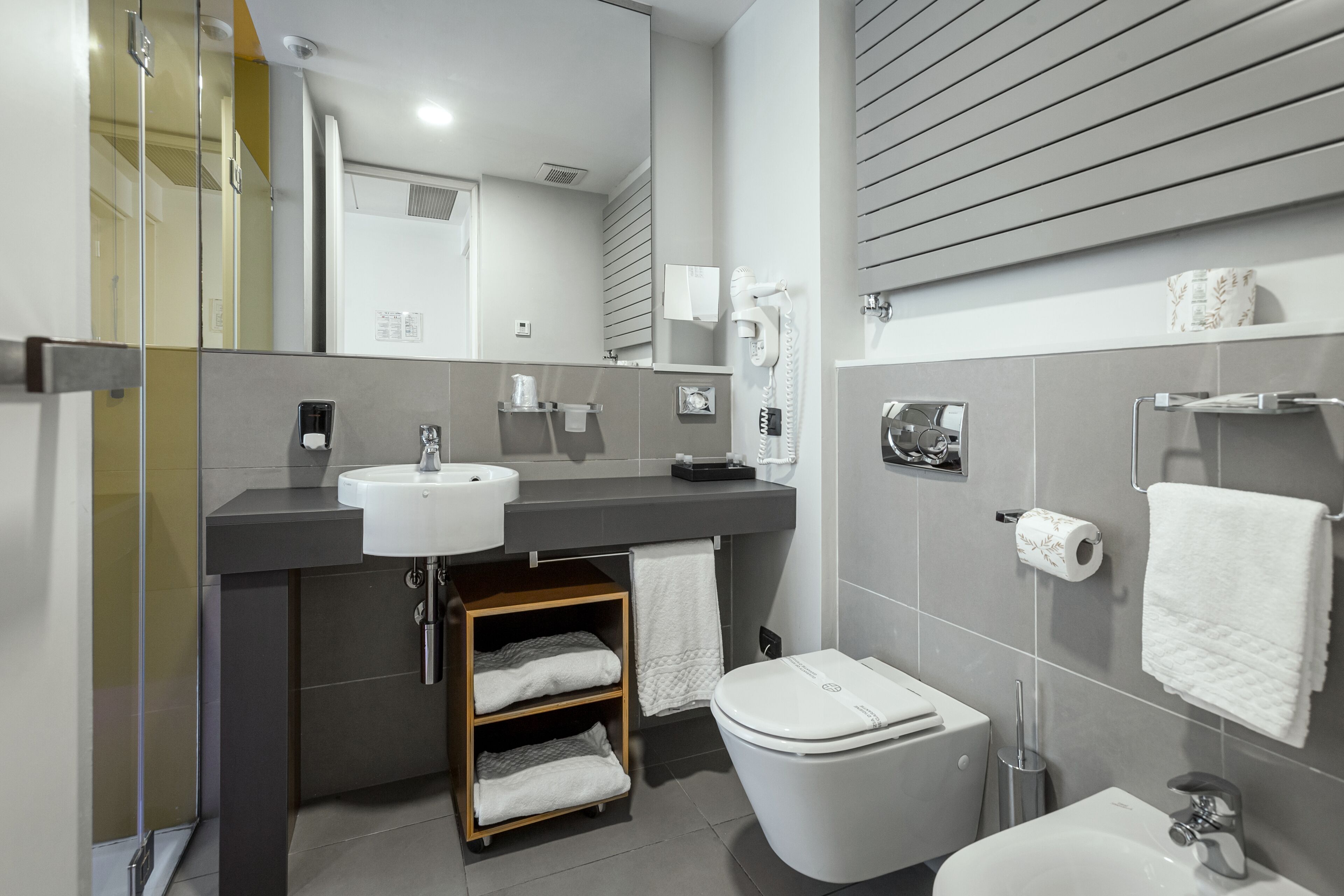 A modern bathroom with a large mirror, a sink, a toilet, and a shower area.