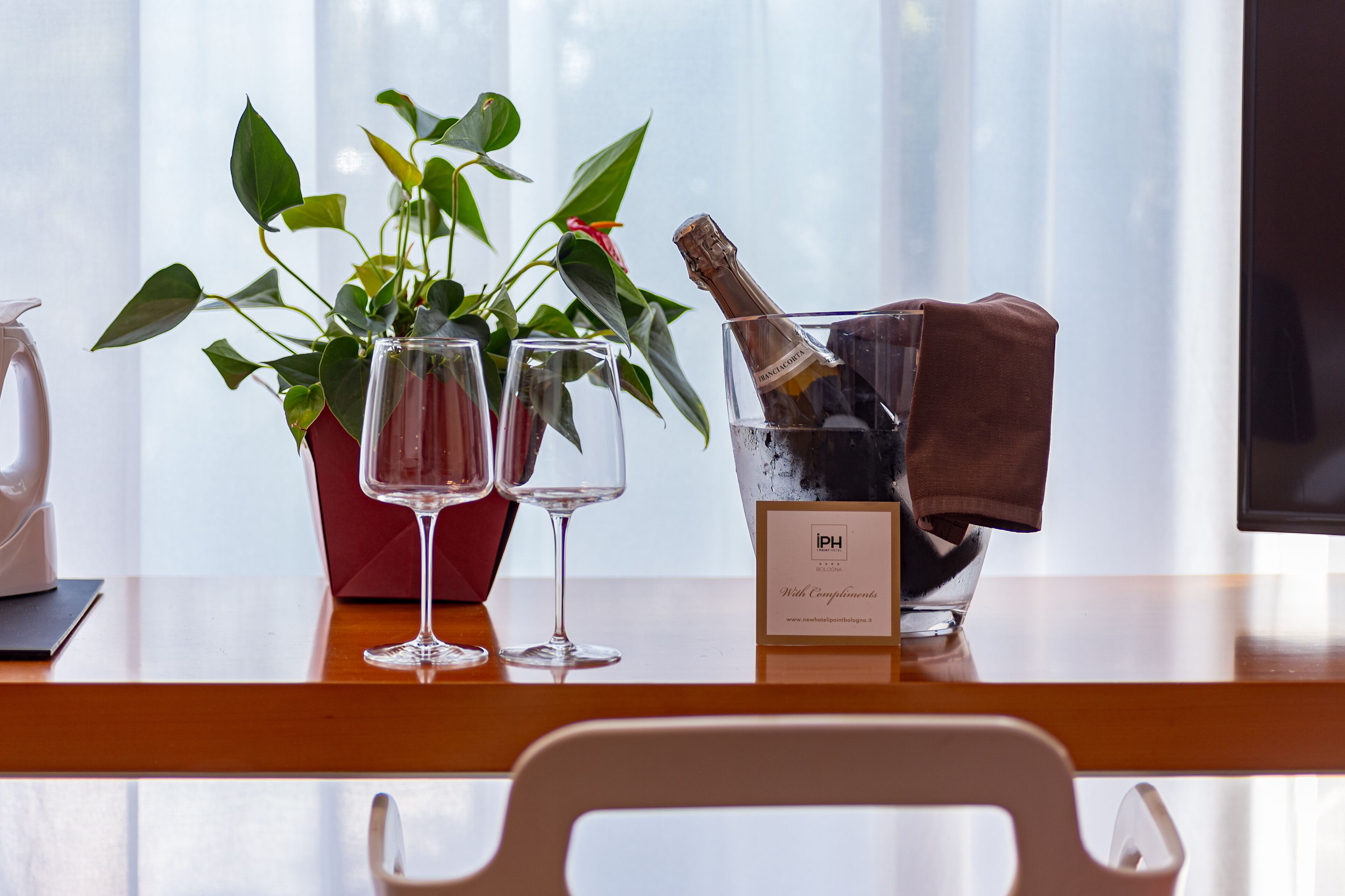 A table with a potted plant, two empty wine glasses, a bottle of champagne, and a sign with the initials "PH".