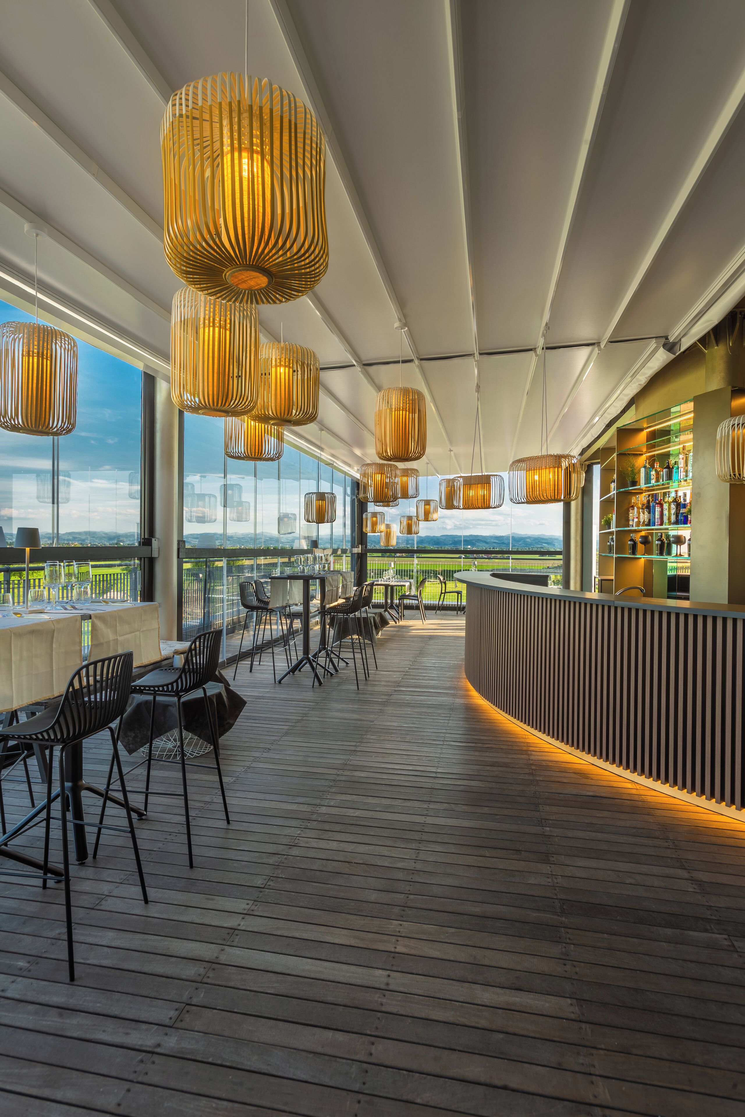 Uma área de bar moderna com um deck de madeira, cadeiras pretas e luminárias pendentes.