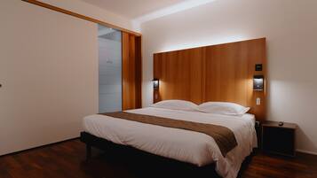 Une chambre moderne avec une tête de lit en bois, une table de chevet avec une télécommande et une porte coulissante sur le côté gauche.